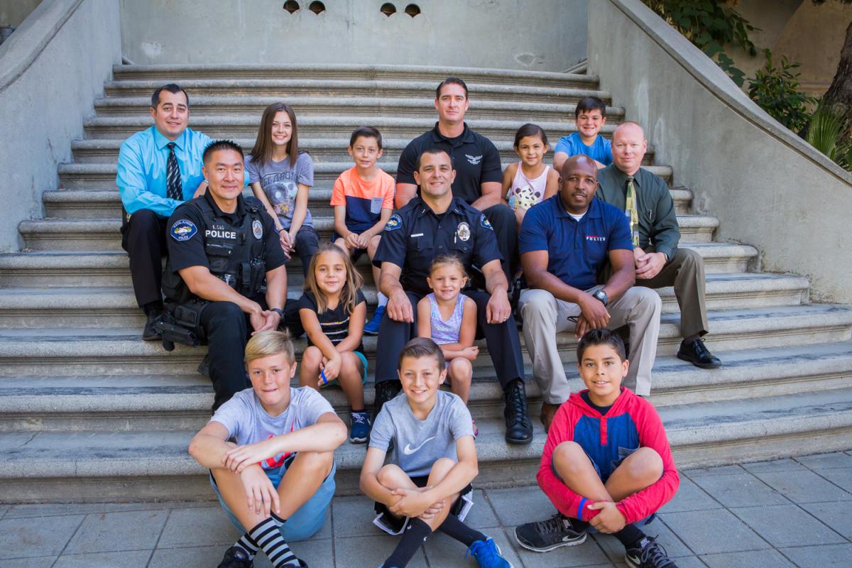 Members of the City of Redlands Police Department sitting on steps with children from the community. 
