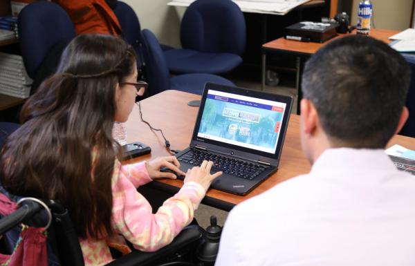 A girl in a motorized wheelchair works on a laptop.