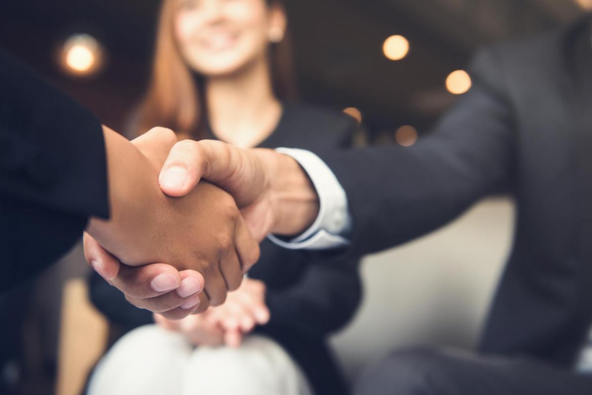 Two people shaking hands with an onlooker.