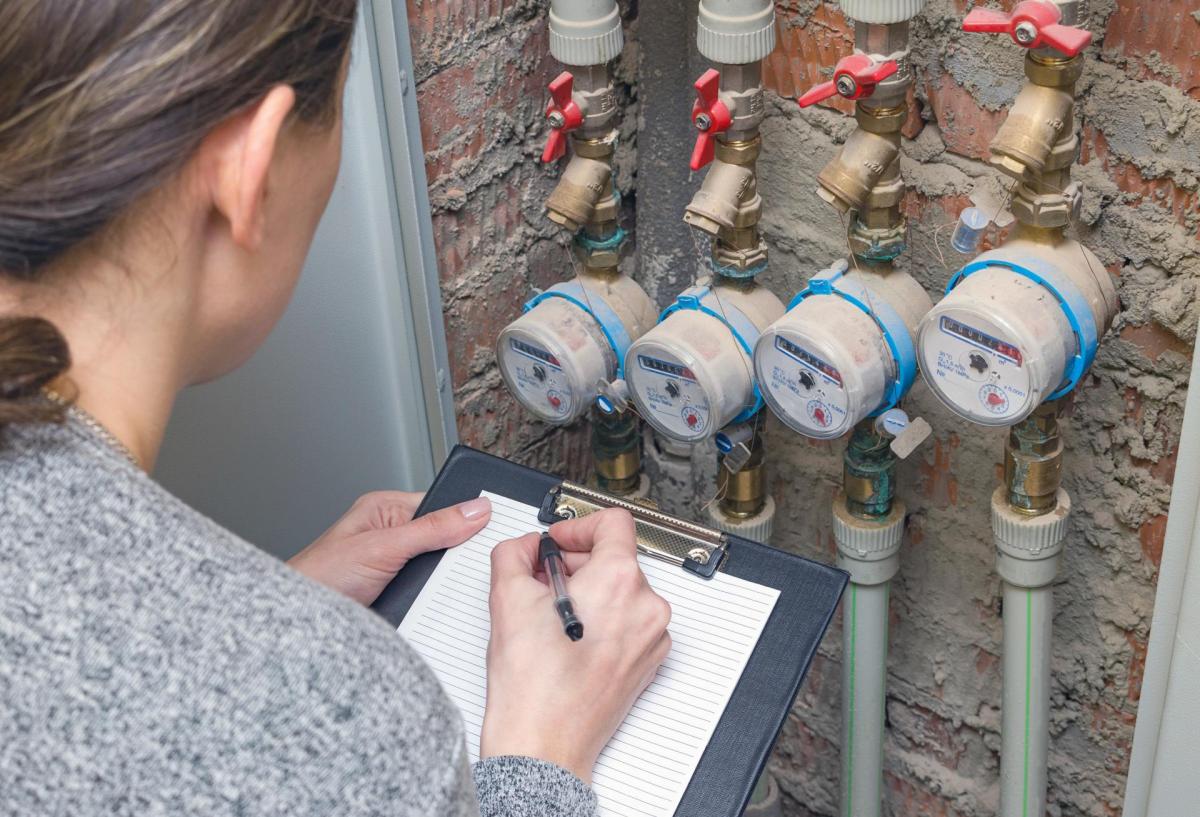 Woman reading water meters on the side of a building.