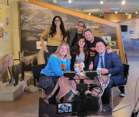 A group of men and women posing for a picture next to podcasting equipment and cardboard cutouts of wildlife.